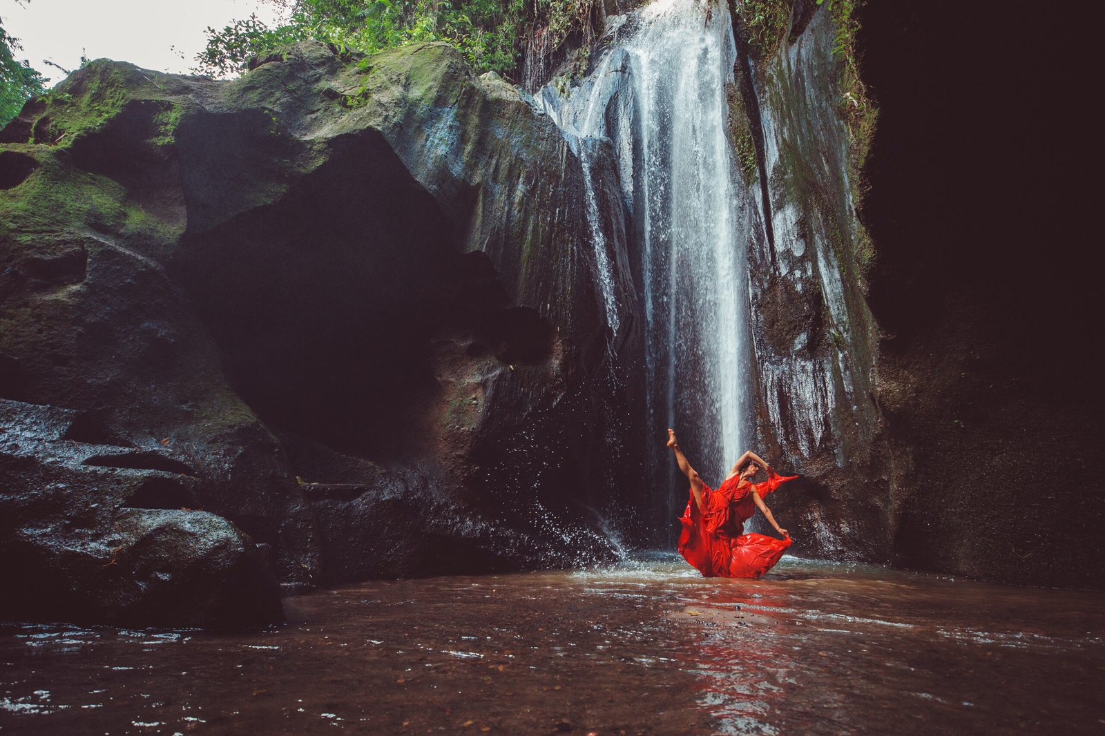 girl in a red dress dancing in a waterfall.